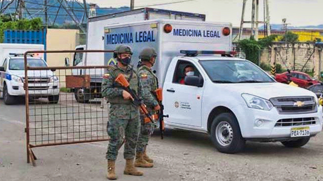 Two Ecuadorian military men stand on guard with rifles as a medicine truck passes by.