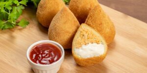 Brazilian deep fried coxhinhas on a cutting board or table with red dipping sauce, like ketchup are delicious and are part of the Brazilian expierence.