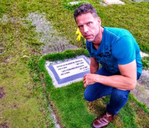 Eric squatting next to Griselda Blanco's grave in Itagüí, Antioquia Colombia just outside Medellín on a cloudy day.