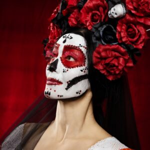 Woman with white, black and red face paint dressed as a catrina with a red and black head dress.
