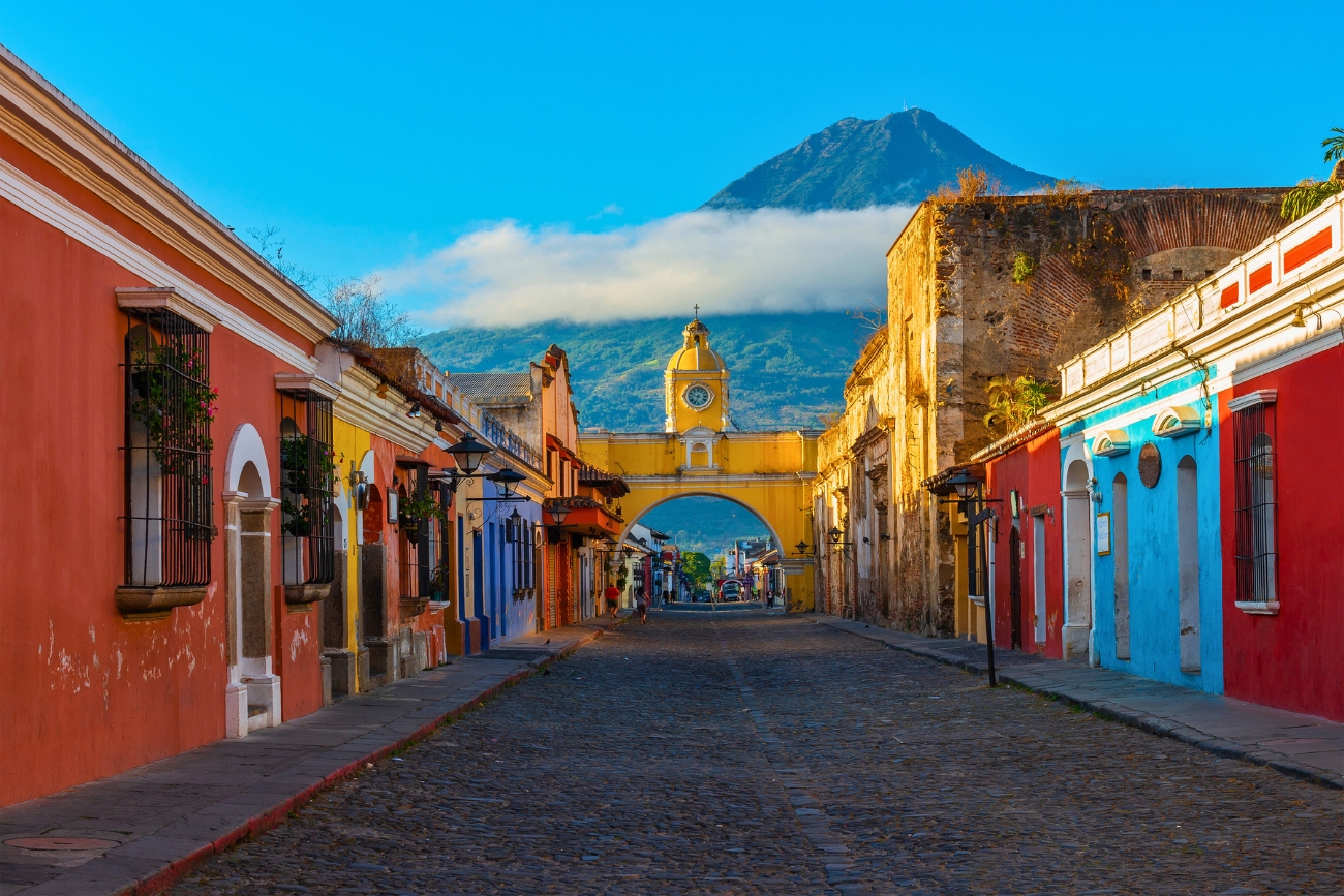 Cityscape of Antigua Guatemala with Santa Catalina in the foreground and the Agua Volcano in the background at sunrise.