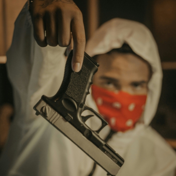 Gangster wearing a white hoodie with red bandana holding a semi-automatic pistol upside down.