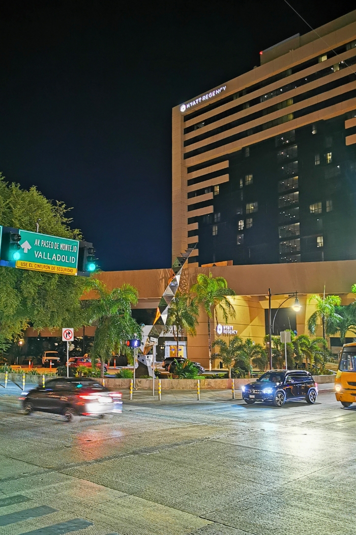 Night photo of the Hyatt Regency showing a green traffic sign toward Valladolid and Paseo Montejo and three cars in Mérida, Yucatán, Mexico.