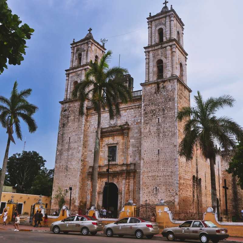San Servacio church in Valladolid, Yucatán with palm trees and taxis waiting near the entrance.