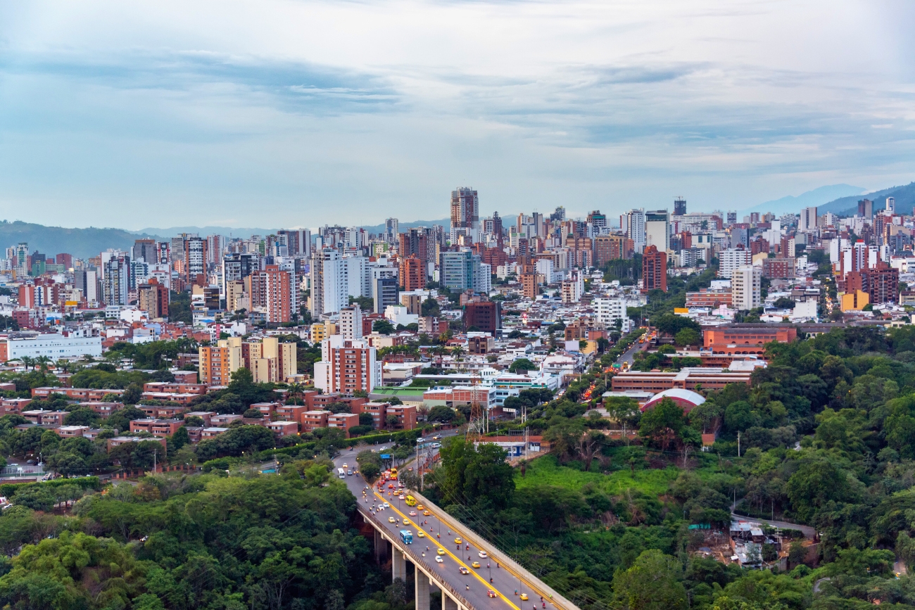 Aerial cityscape of a bridge with cars, verdant trees, and mix of mostly white and brick-red tall buildings in Bucaramanga, Santander, Colombia.