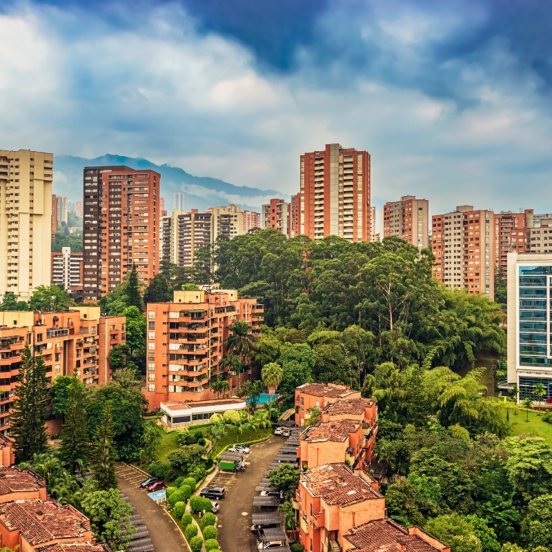 Aerial cityscape of El Poblado neighborhood with verdant landscape, partly cloudy skies and tall brick-red buildings in Medellín, Antioquia, Colombia.