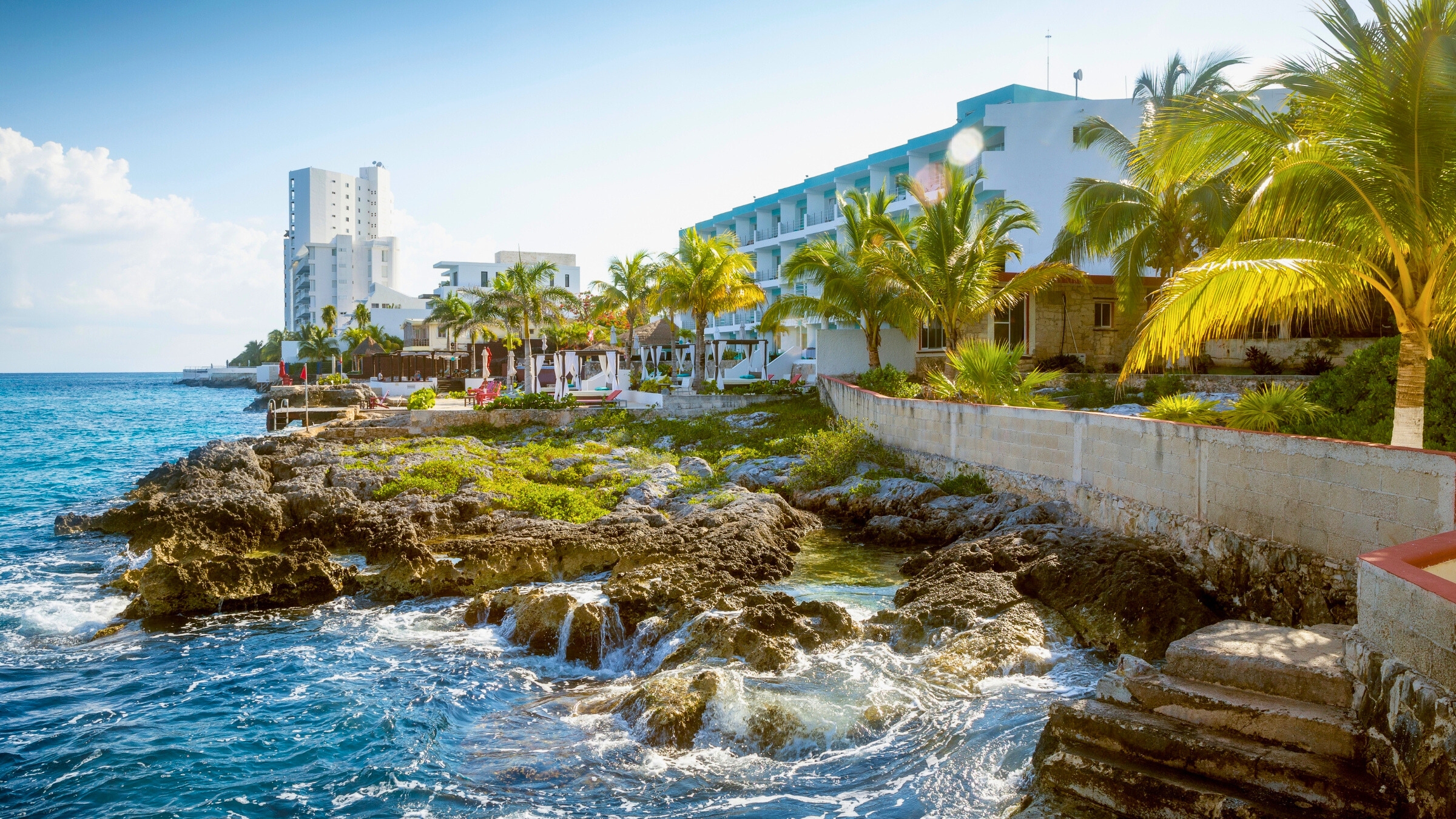 Gorgeous blue water and mostly blue skies along with hotels shown along the rocky shore of Cozumel, Quintana Roo, Mexico.