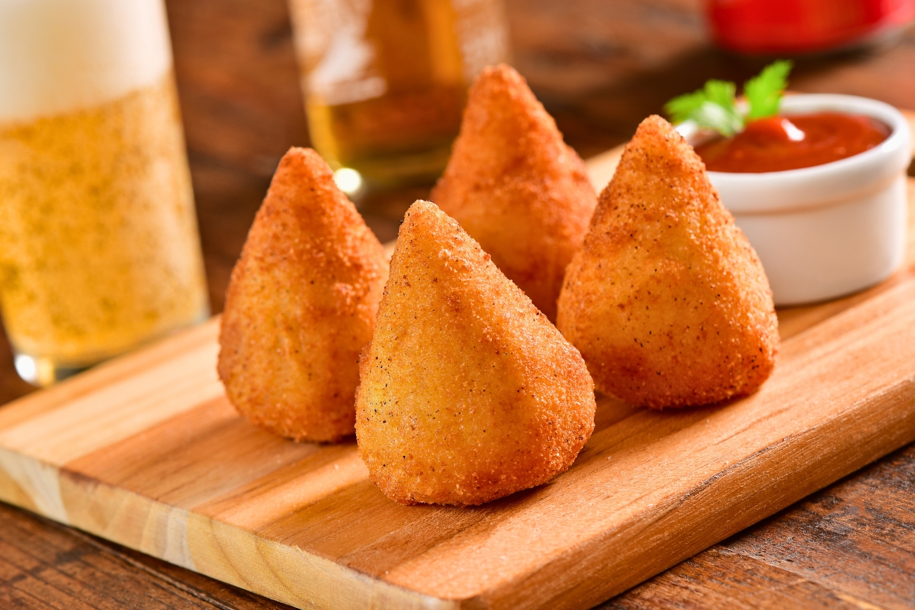 Brazilian deep fried coxinhas on a cutting board or table with red dipping sauce, like ketchup are delicious and are part of the Brazilian experience.