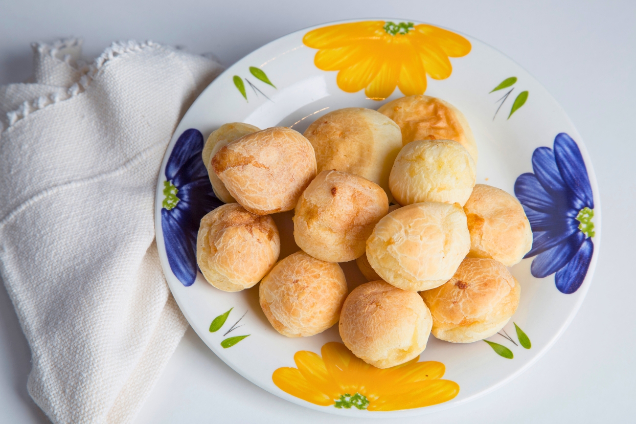 Pão de queijo served on a white dish designed with yellow and bluish flowers.