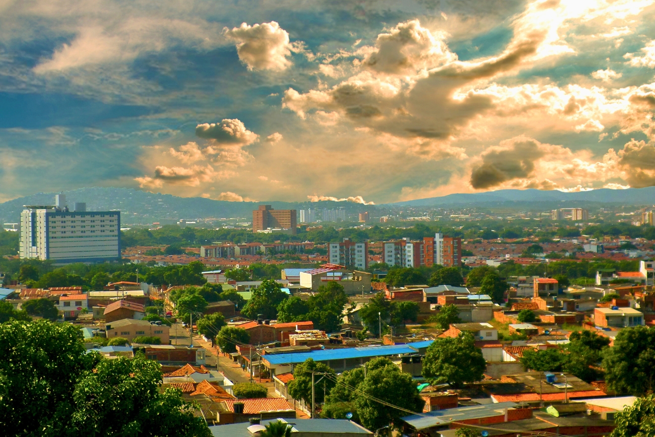 Various buildings with brick-red roofs shown from above with green vegetation on a partly cloudy day at sunset in Cúcuta, Norte de Santander, Colombia.