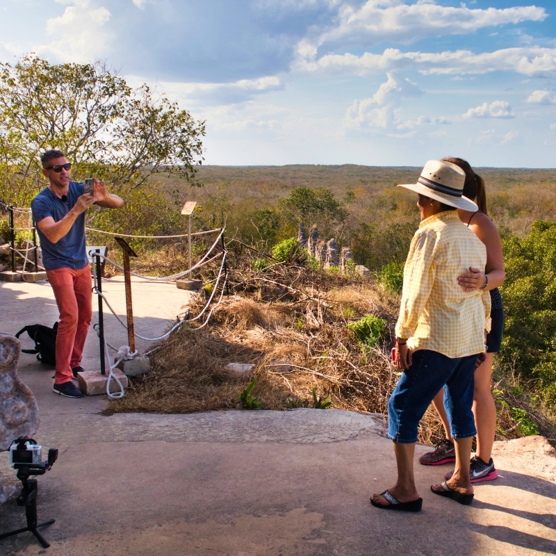 Eric taking photo of 2 female tourists atop Templo Mayor in Uxmal, Yucatán, Mexico on a sunny day.