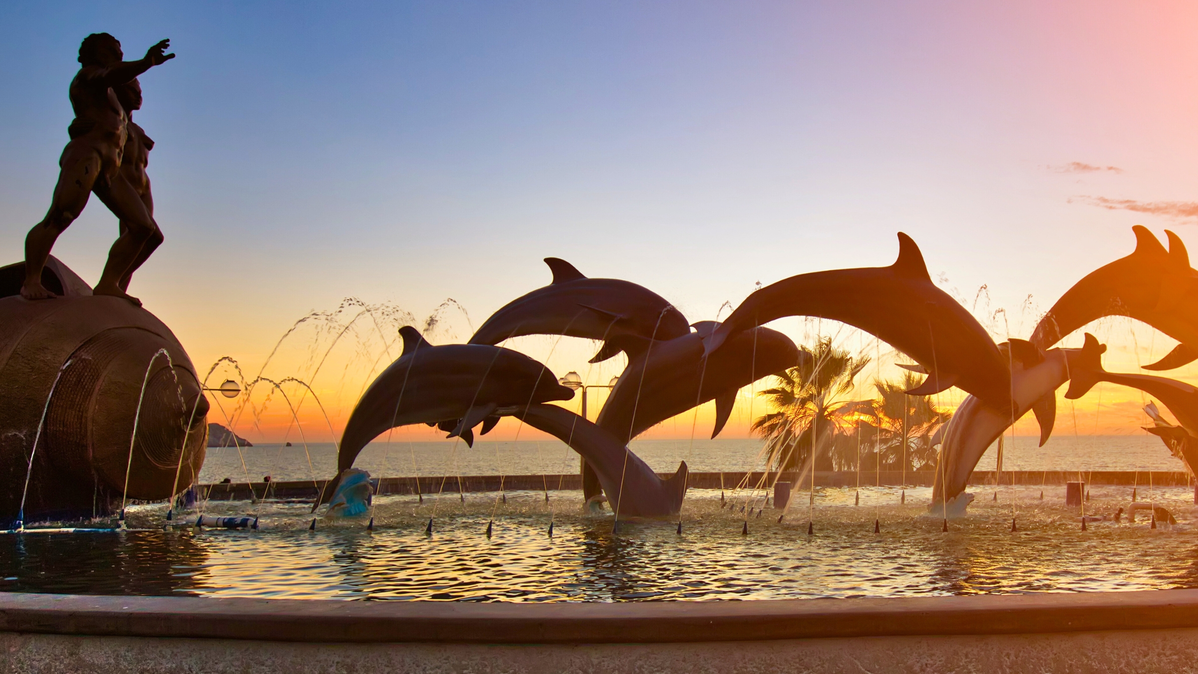 Statue of a seaman and dolphins jumping at golden hour on the malecón in Mazatlán, Sinaloa, Mexico.