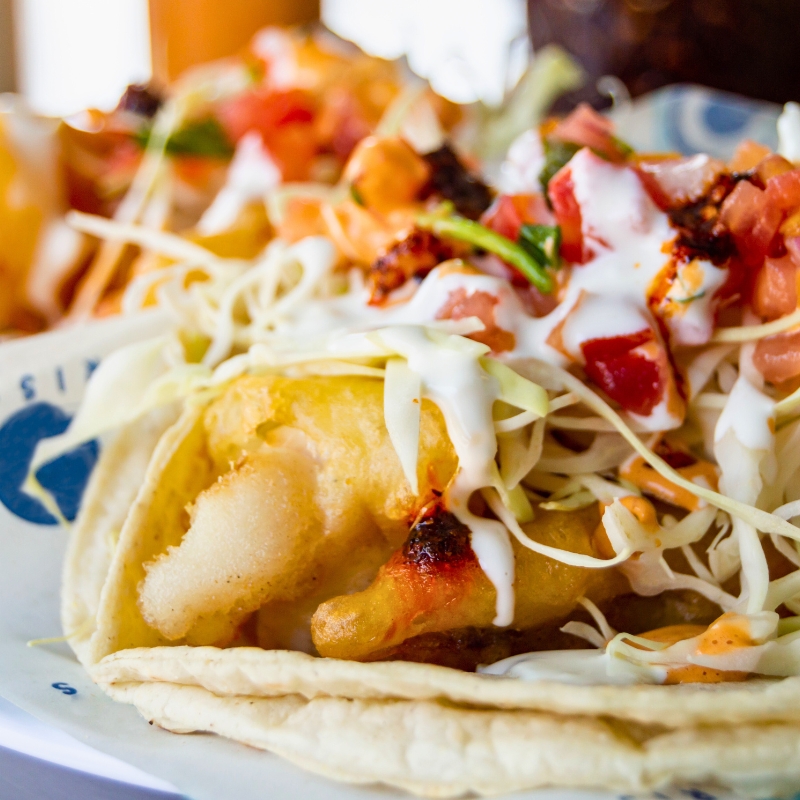 Seafood tacos with cabbage, cilantro, sour cream, tomatoes on a double flour tortilla.