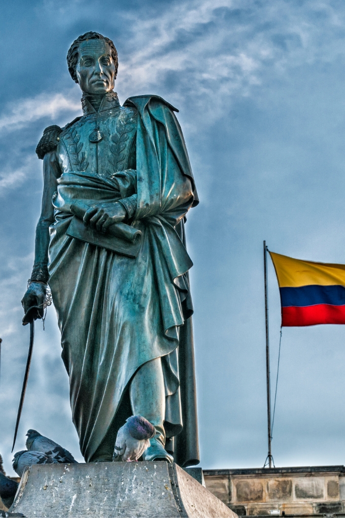 Statue of Simon Bolívar with Colombian flag waving in background in Bogotá, DC, Colombia.