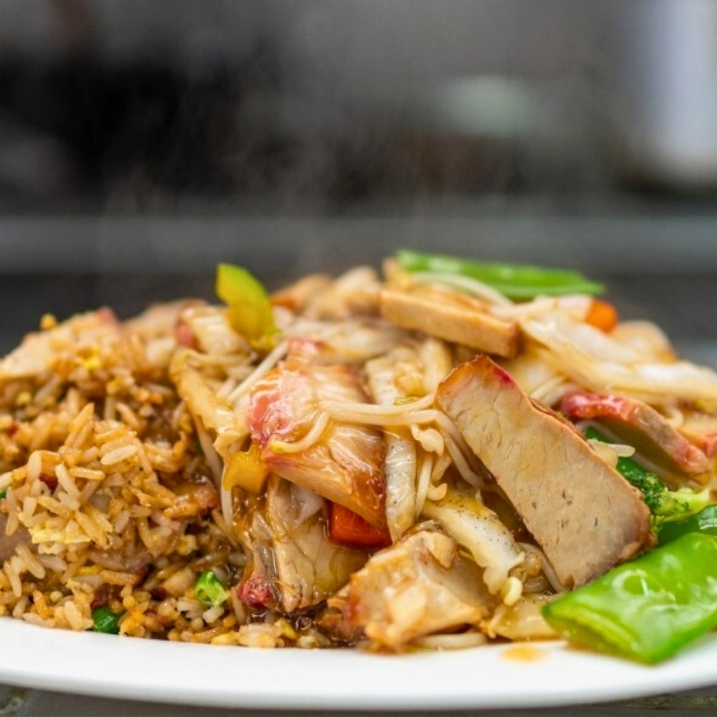 Ecuadorian/Peruvian cuisine, "chifa" showing pork chaufa with rice (with soy sauce mixed in) noodles, and scallions on a white plate on a grey table with steam rising from the plate.