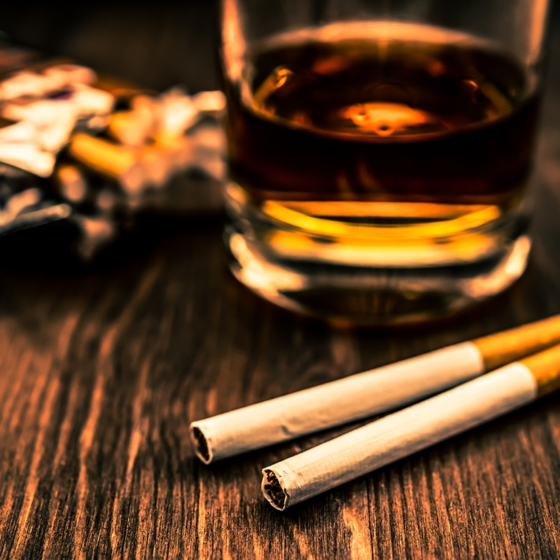 2 unlit cigarattes in front of a glass of whisky or scotch.