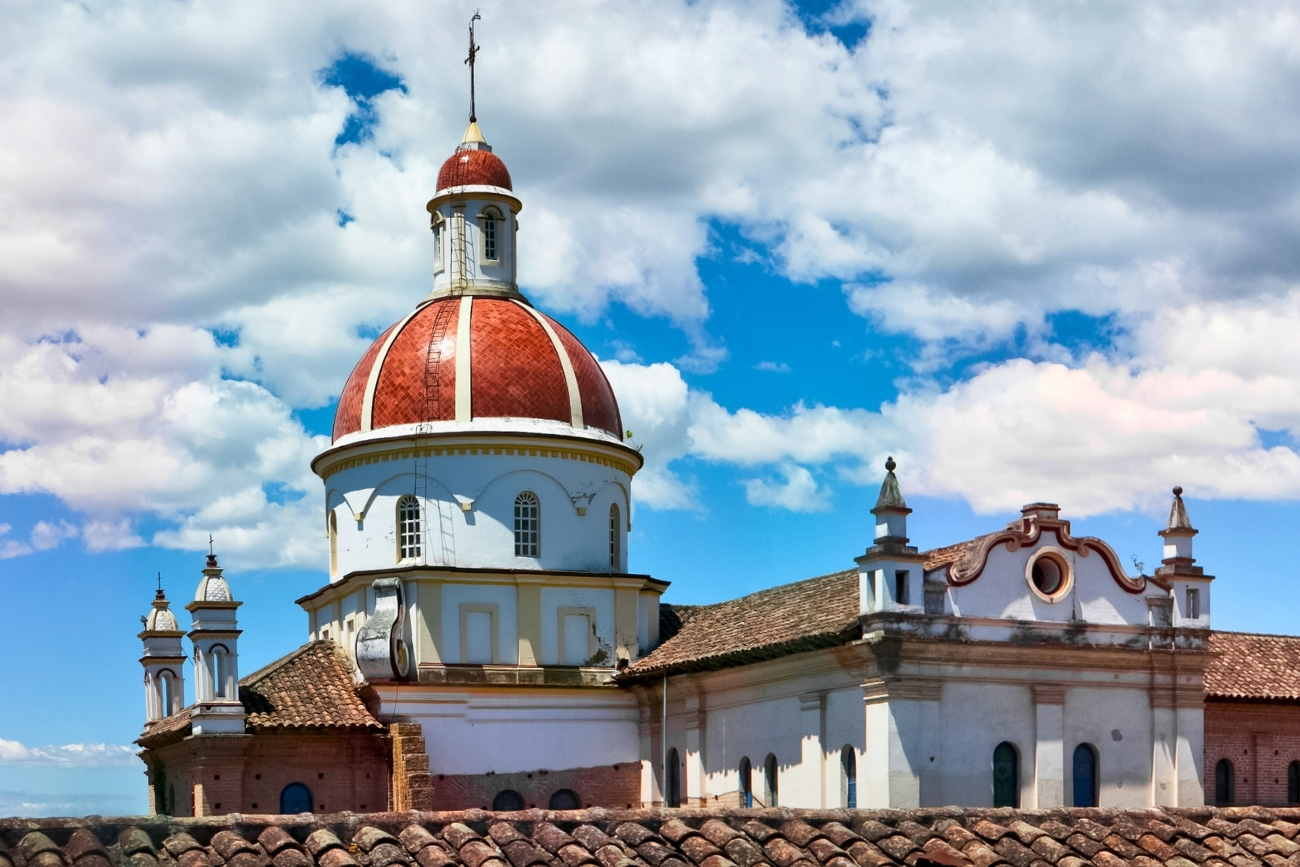 White church with cafe colored dome with a sunny, partly cloudy background in Cotacachi, Ecuador.