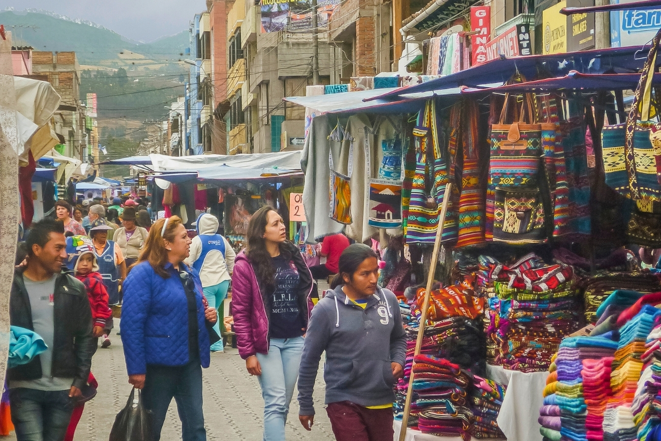 A bustling city market with people looking at woven, colorful textiles in Otavalo, Ecuador on an overcast day.